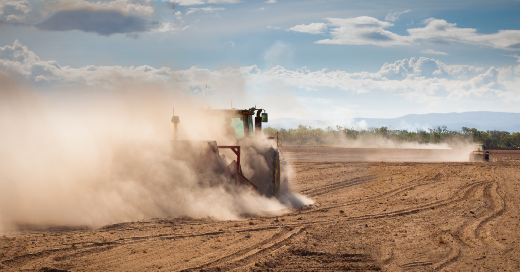 A tractor engulfed in a cloud of dust while is plowing